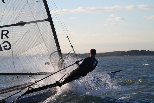 Dinghy sailor hiked out hard, spray flying