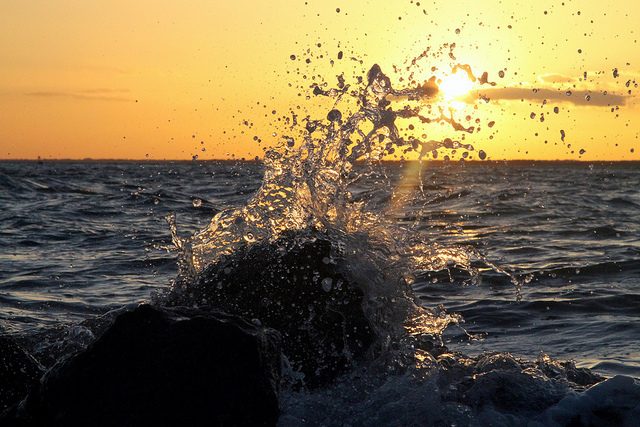 Wave crashing over rocks at sunset
