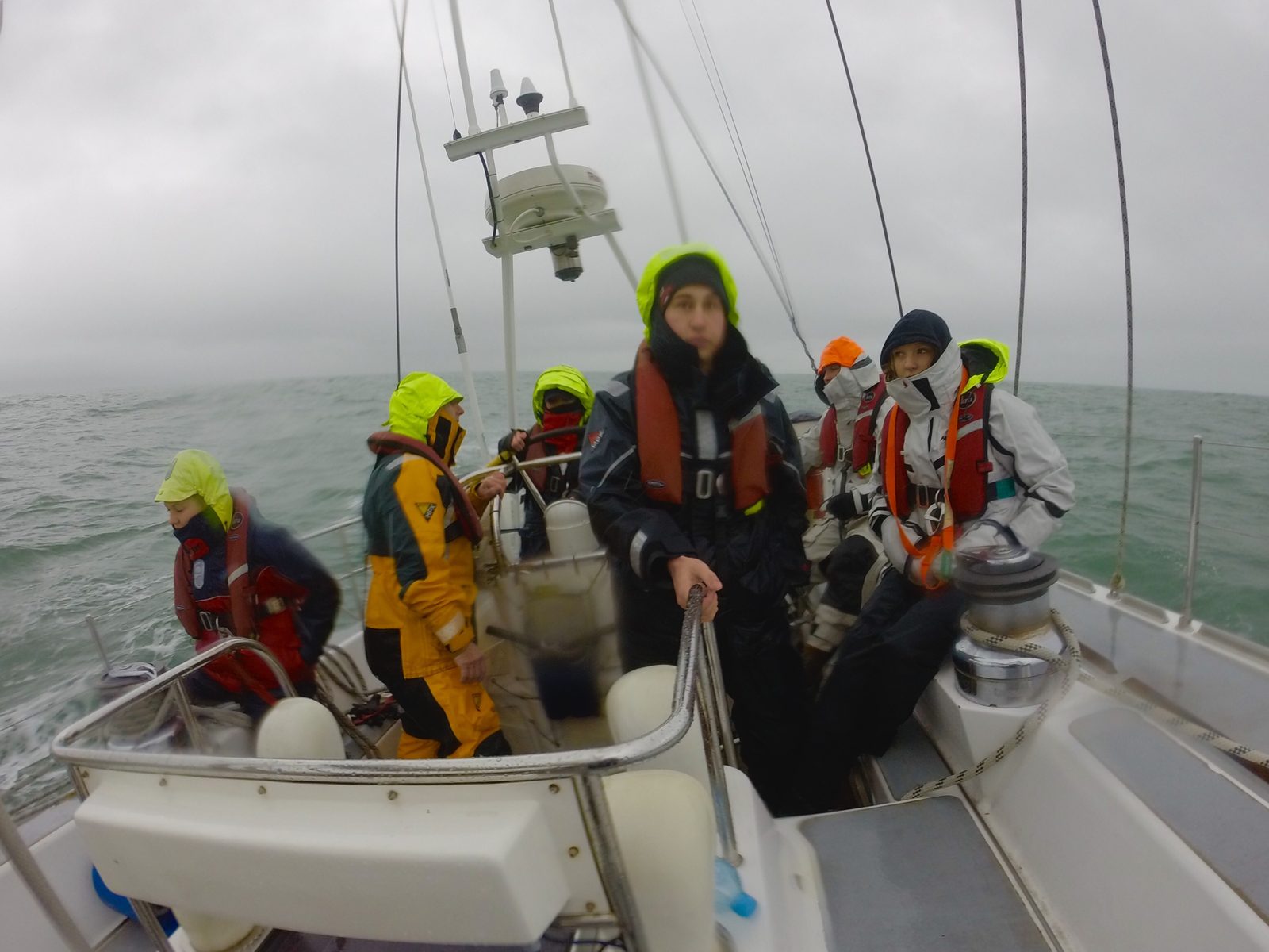 Crew in foul-weather gear on a yacht in grey conditions
