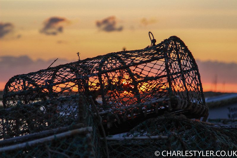 Silhouetted lobster pots against an orange sunset over the sea at Brancaster Staithe, Norfolk
